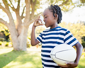 Young African-American boy holding a volleyball and using his asthma inhaler outside